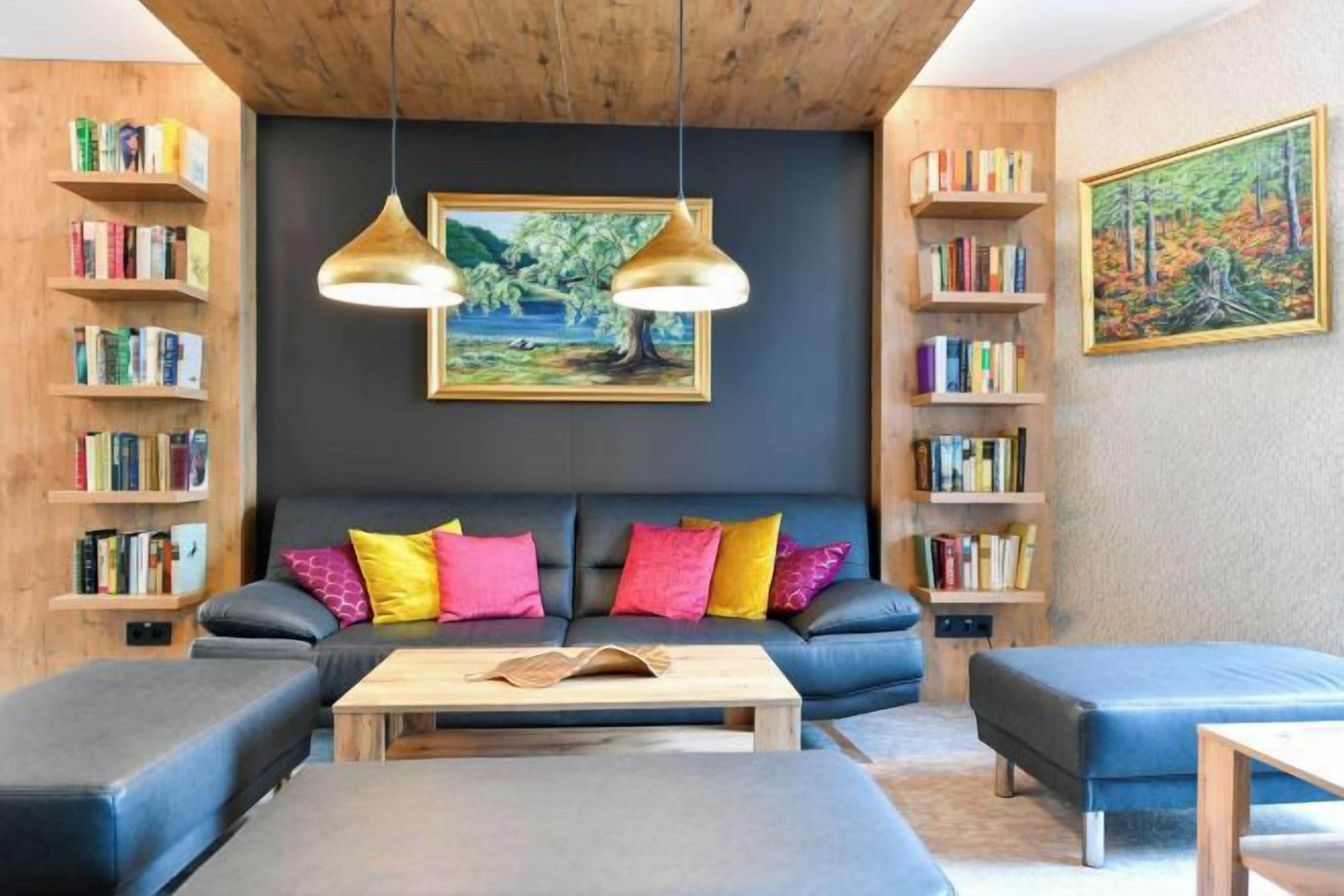 Un saló d'estar acollidor amb un sofà, un pouf i una taula de centre, envoltat d'estanteries i dues pintures.