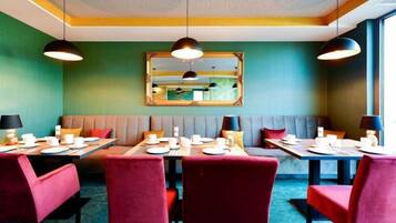 Un comedor con mesas dispuestas para cuatro, un espejo grande en la pared y una pared verde.