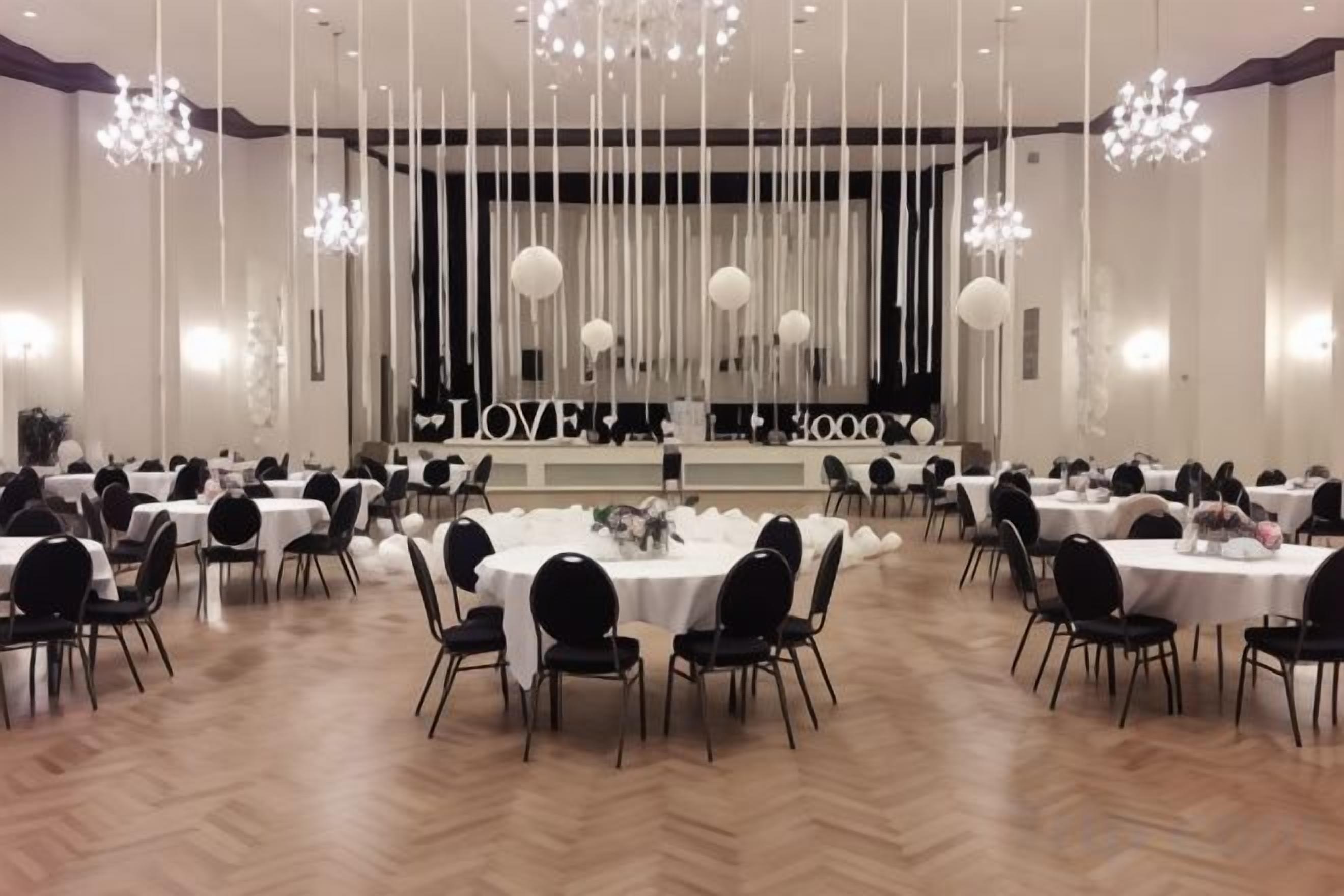 Un salón de banquetes con varias mesas redondas, sillas y un escenario con un telón de fondo.