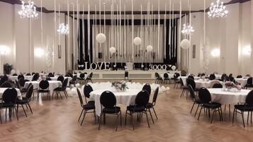 Un salón de banquetes con varias mesas redondas, sillas y un escenario con un telón de fondo.