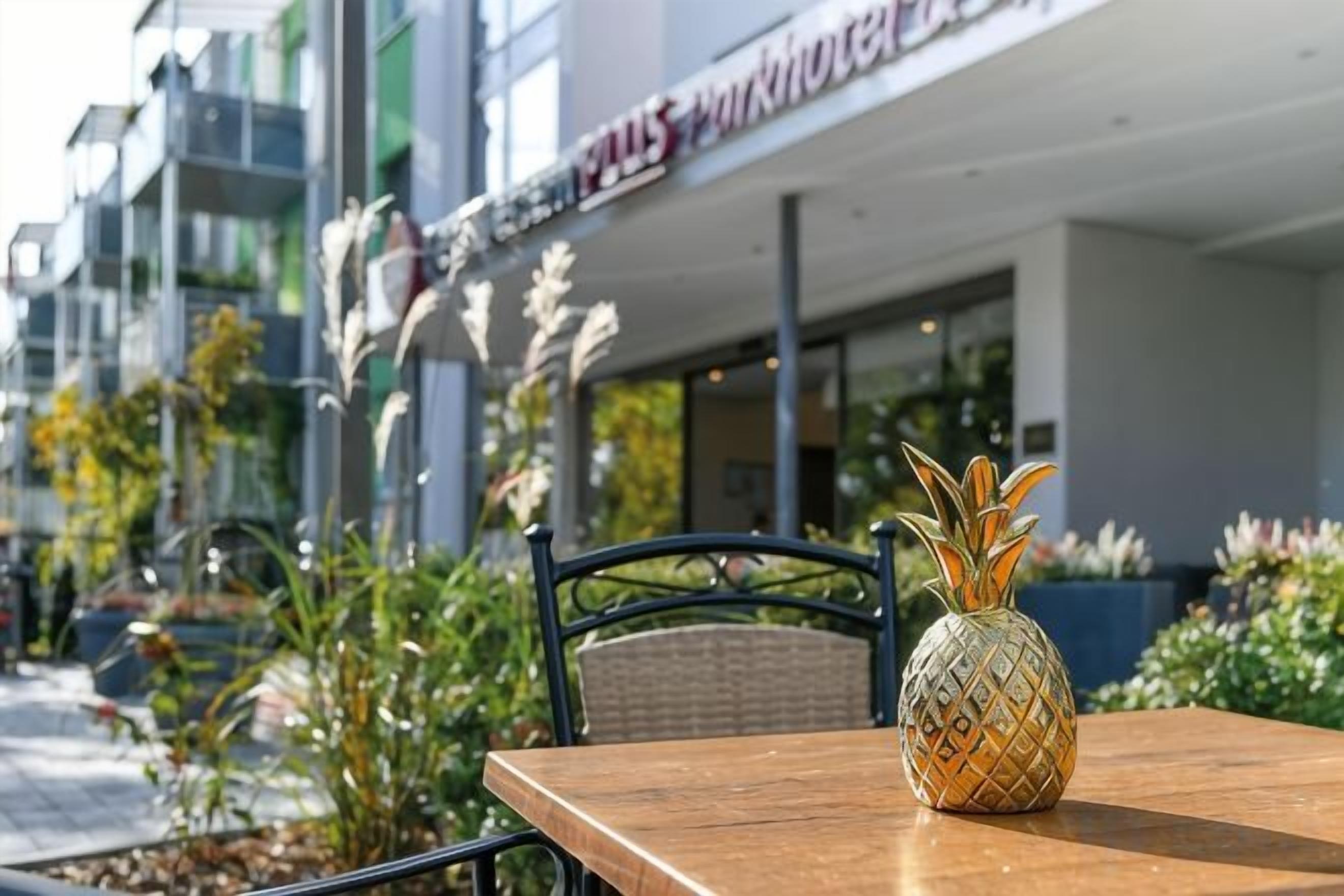 A wooden table with a pineapple centerpiece, a wicker chair, and a building with a sign that reads 'PULLMAN HOTEL' in the background.