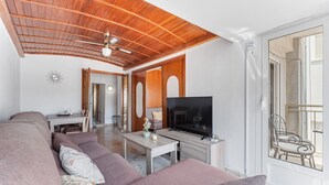 A living room with a sofa, TV, wooden ceiling, and a view through a glass door.