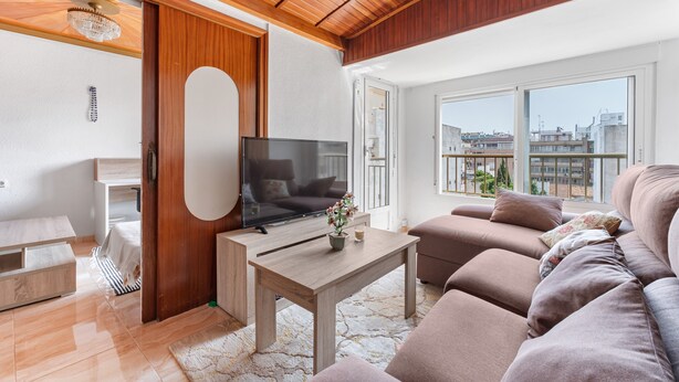 A modern living room with a flat-screen TV, wooden ceiling, and a balcony with a city view.