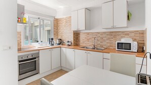 A modern kitchen with white cabinets, a microwave, a sink, and a window.