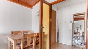 A dining area with a wooden table and chairs, a sliding door with a golden panel, and a view into a living space with a sofa and a glass table.