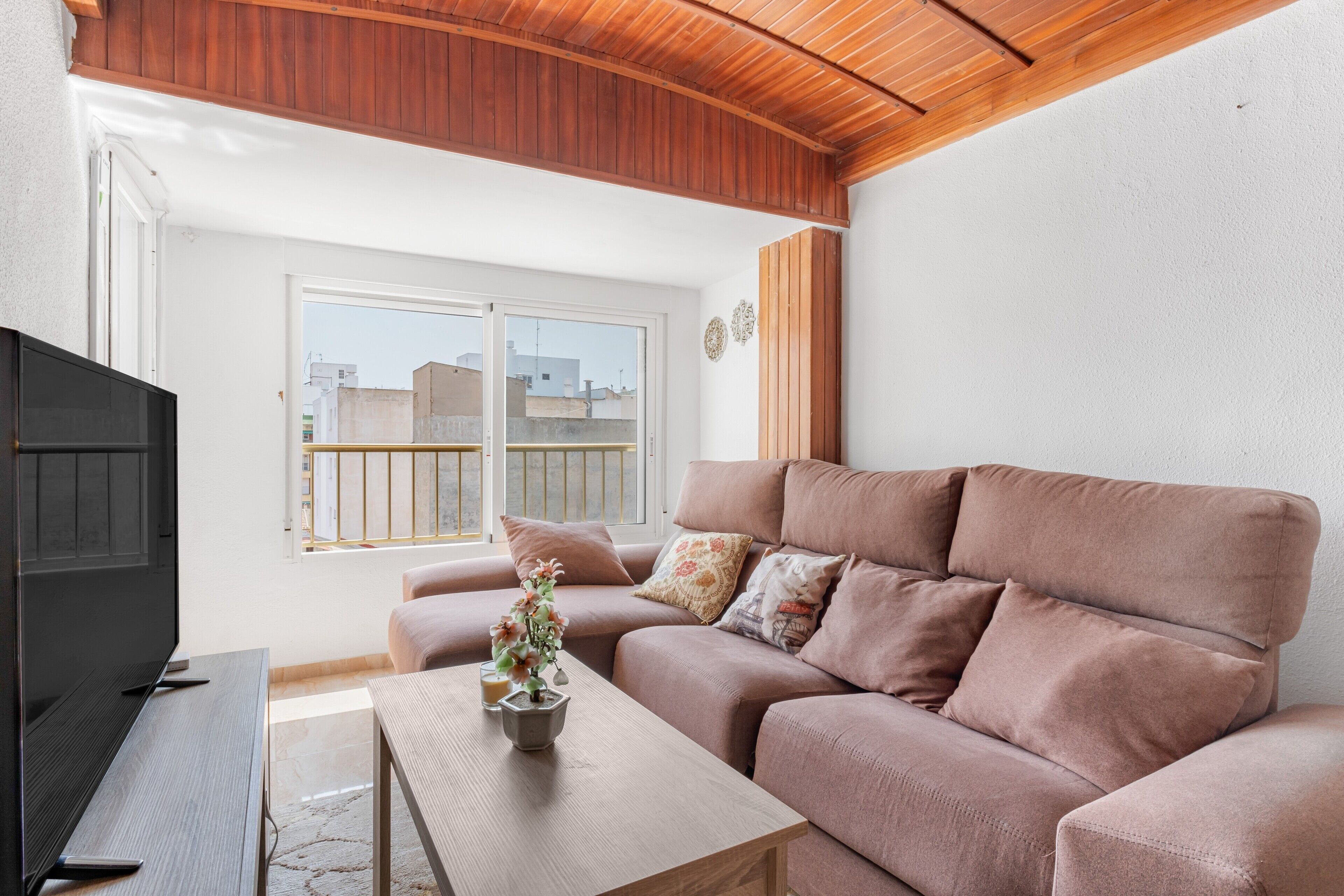 A living room with a sofa, a coffee table with a plant, a TV, and a window with a view of buildings.