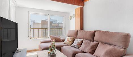 A living room with a sofa, a coffee table with a plant, a TV, and a window with a view of buildings.