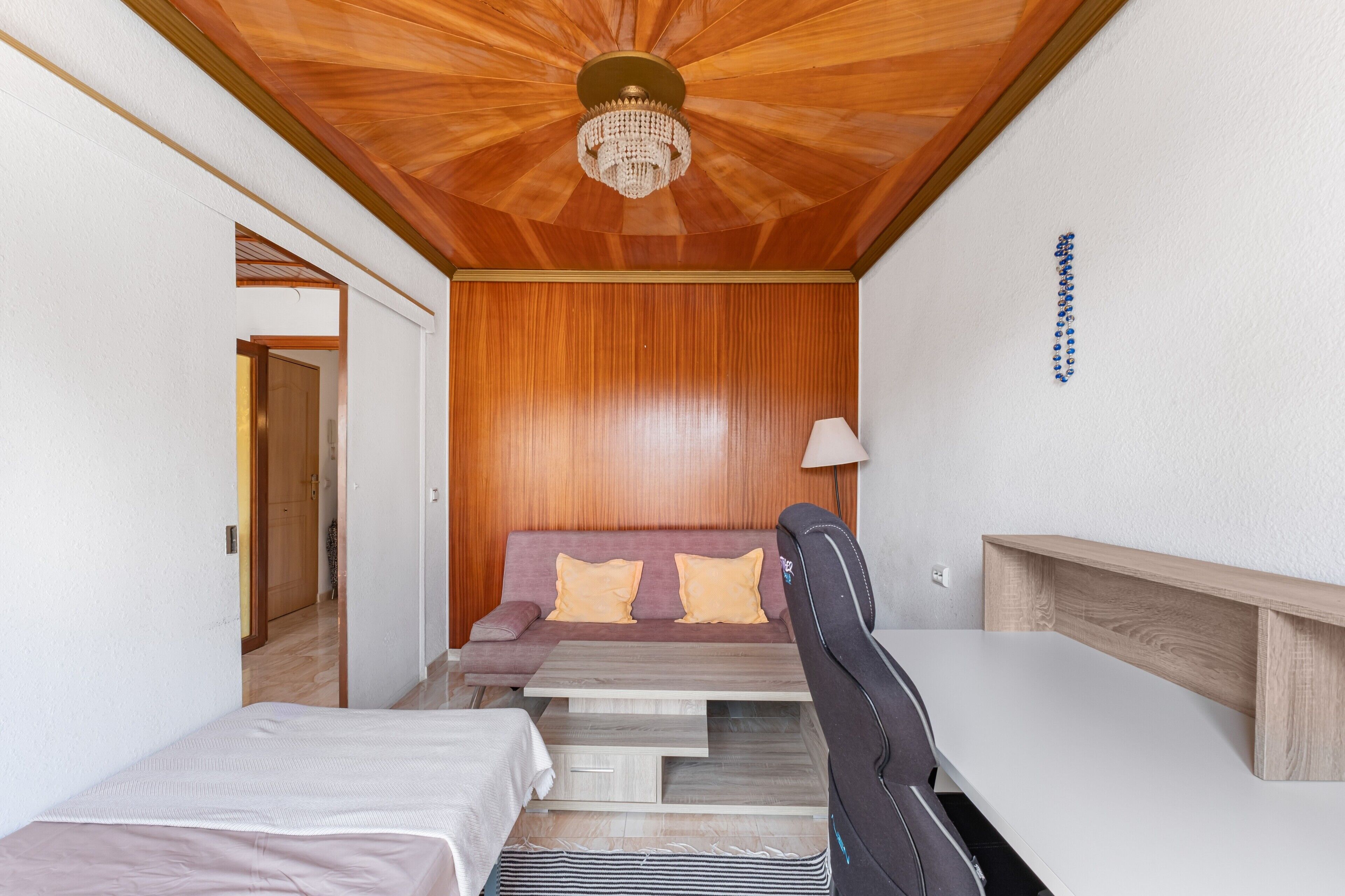 Una habitación compacta con techo de madera, un sofá con cojines, una cama, un escritorio y una lámpara.