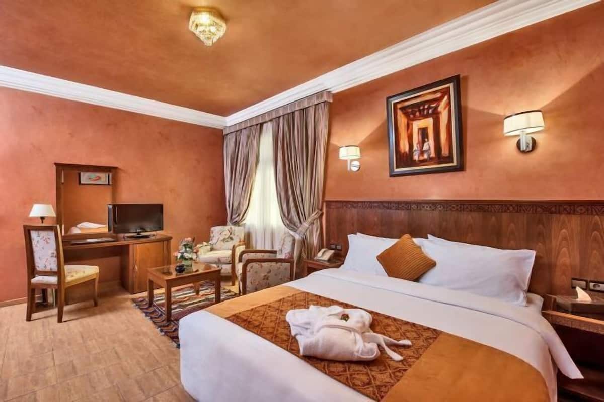 Une chambre d’hôtel avec un lit, un bureau doté d’une télévision, une chaise, une lampe et un tableau au mur.