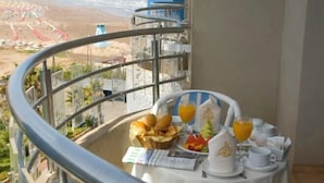 Un balcon avec une table préparée pour le petit-déjeuner, donnant sur une plage parsemée de parasols.