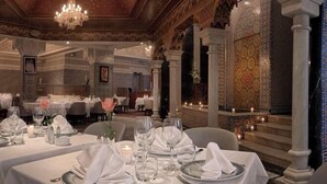Une salle à manger avec des tables dressées pour le service, des colonnes richement décorées et un mur orné de motifs.