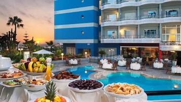 A poolside buffet with various food items and a pool in the background.
