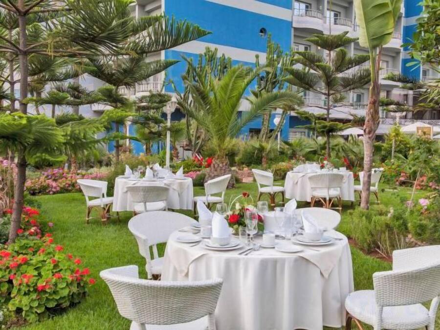 An outdoor dining area with round tables set for guests, surrounded by lush greenery and tropical plants.
