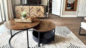 A modern living room with a herringbone-patterned wooden cabinet, a flat-screen TV, and a round coffee table with a woven tray.