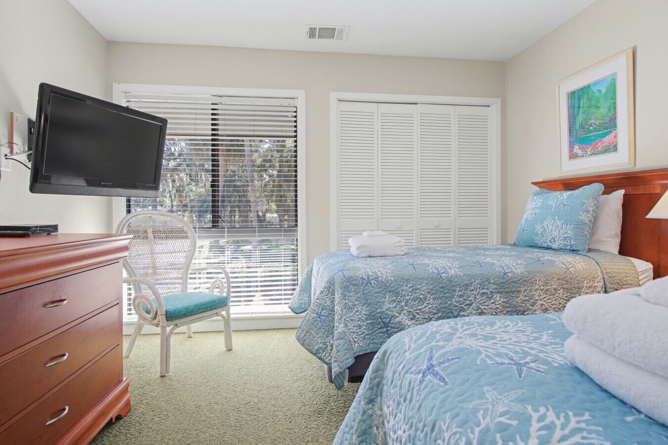Quarto de hotel com duas camas, televisão, uma cadeira e janela com persianas.