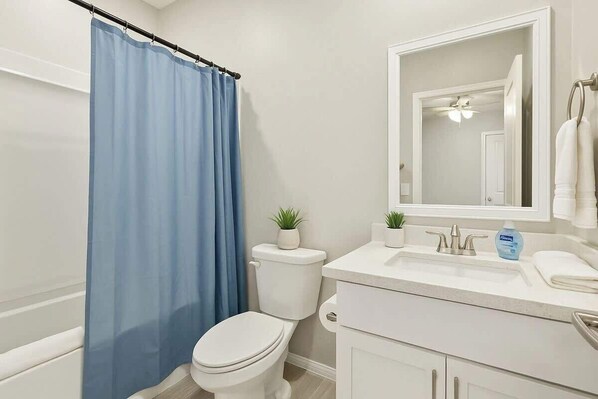 A bathroom with a white toilet, a blue shower curtain, a white sink with a mirror above it, and a small potted plant on the counter.