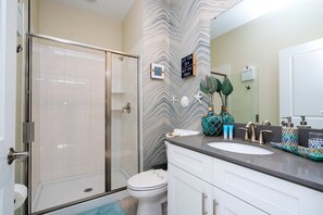 Un baño con cabina de ducha de vidrio, inodoro blanco, lavamanos con encimera de mármol y elementos decorativos como estrellas de mar y una planta en maceta.