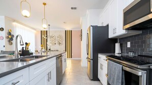 A modern kitchen with white cabinets, stainless steel appliances, and pendant lighting. - Magical Stay Mickey and Harry Potter Rooms (Kissimmee)