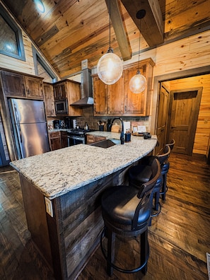 A kitchen with wooden cabinets, a stainless steel refrigerator, a granite countertop, and a bar area with stools. - Sauna/Massage Chair/Hot Tub/Privacy/Paved Roads (Broken Bow)