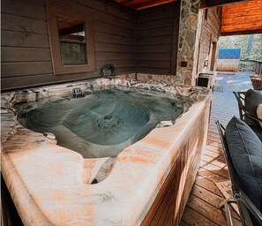 Una vasca idromassaggio in una baita di legno con pareti in pietra e un pontile in legno.