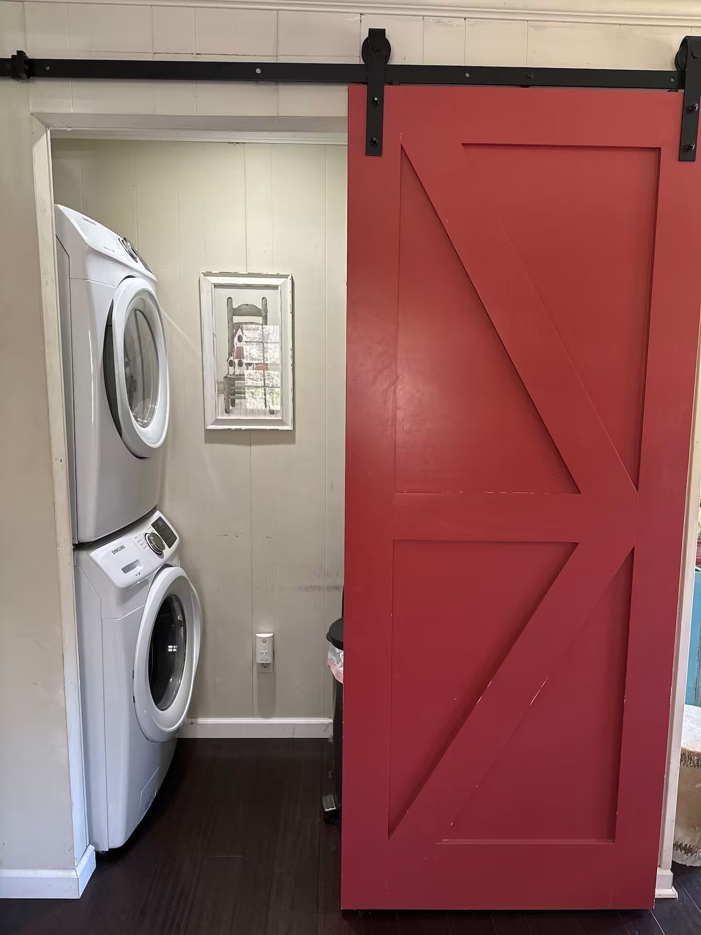 A laundry room with a red door, a white washing machine, and a framed picture on the wall.