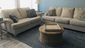 A living room with two beige sofas, a wicker ottoman, and a framed picture on the wall. - SPECIAL PRICES FOR SEPT!  Beachfront Retreat! Monthly specials you can't believe (Panama City Beach)