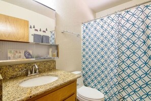 Un baño con lavamanos de encimera de granito, un espejo, toallero y un inodoro.