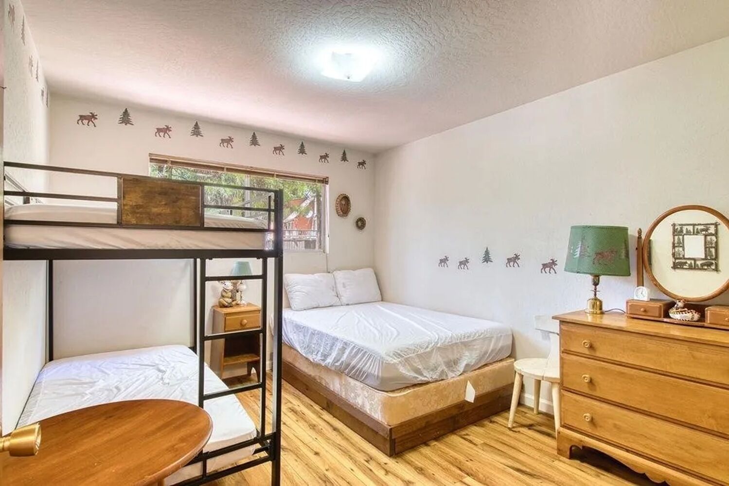 Une chambre avec des lits superposés, un lit simple, une commode, un miroir et des autocollants décoratifs représentant des animaux et des arbres.