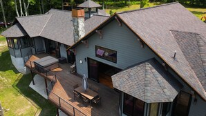 A large, multi-story house with a spacious deck, a stone chimney, and a covered outdoor seating area. - Spacious modern mountain style home with beautiful western views in Corning, NY (Corning)