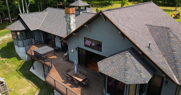 A large, multi-story house with a spacious deck, a stone chimney, and a covered outdoor seating area. - Spacious modern mountain style home with beautiful western views in Corning, NY (Corning)