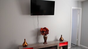 A modern living room with a flat-screen TV mounted on the wall, a wooden entertainment unit with a built-in fireplace, and two decorative vases.