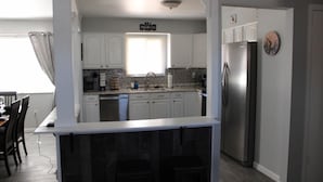 A compact kitchen with white cabinets, a stainless steel refrigerator, and a window with blinds.