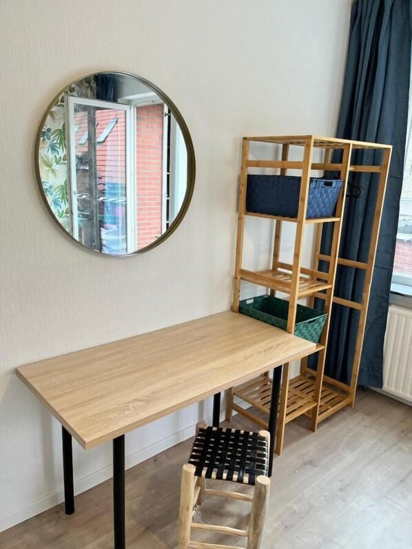 A room with a wooden desk, a chair, a mirror, and a wooden shelving unit with baskets.