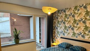Un dormitorio con cama, una planta en maceta, una ventana y una pared con diseño de hojas.