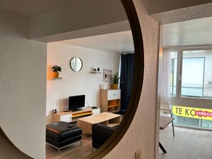 A modern living room with a TV, sofa, coffee table, and a dining area with a chair and table.