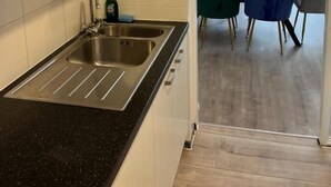 Una cocina moderna con encimera negra, pileta de acero inoxidable y armarios blancos. Cuenta con un comedor con mesa, sillas y ventana con cortinas.