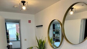 Un área de recepción con un banco de madera, una planta en maceta, un espejo y documentos enmarcados en la pared.