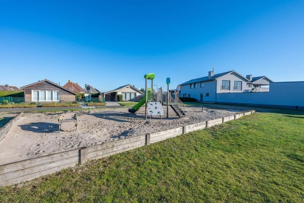 A playground with a slide and climbing structures, surrounded by houses and a grassy area.