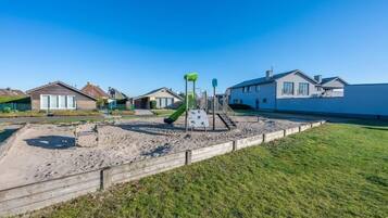 A playground with a slide and climbing structures, surrounded by houses and a grassy area.