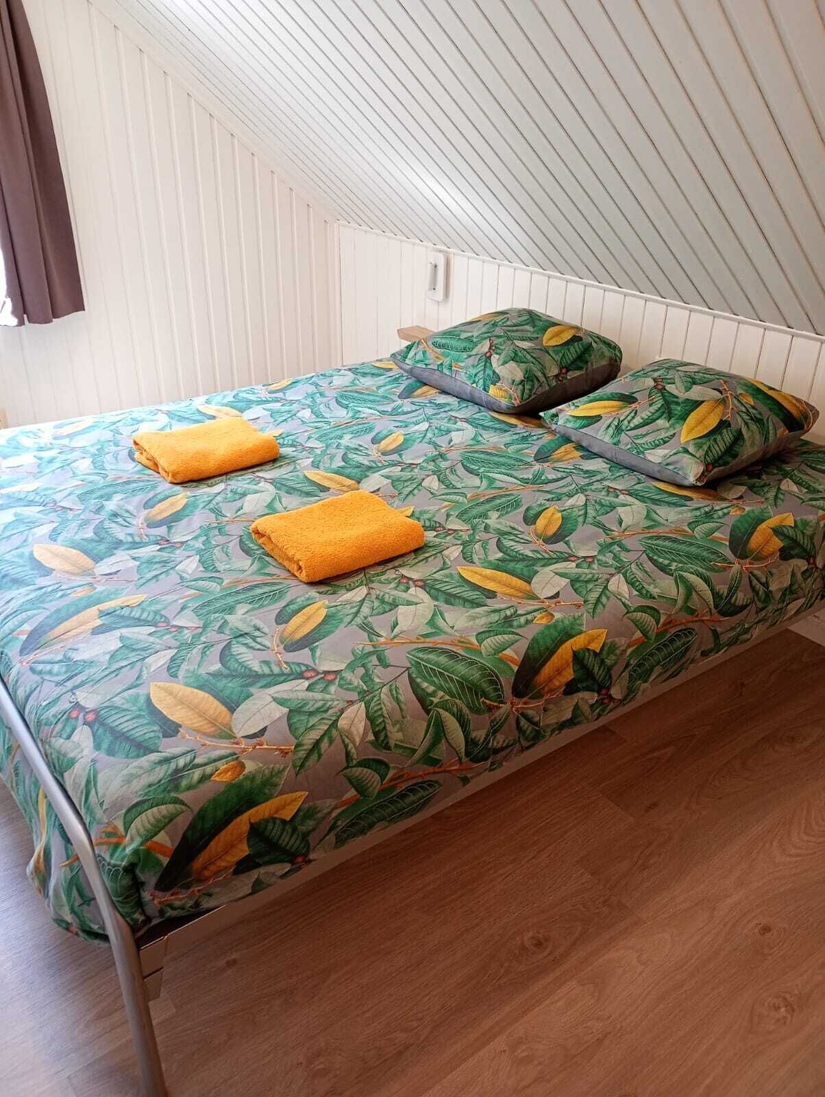 A single bed with a leaf-patterned bedspread, two pillows, and two folded towels.