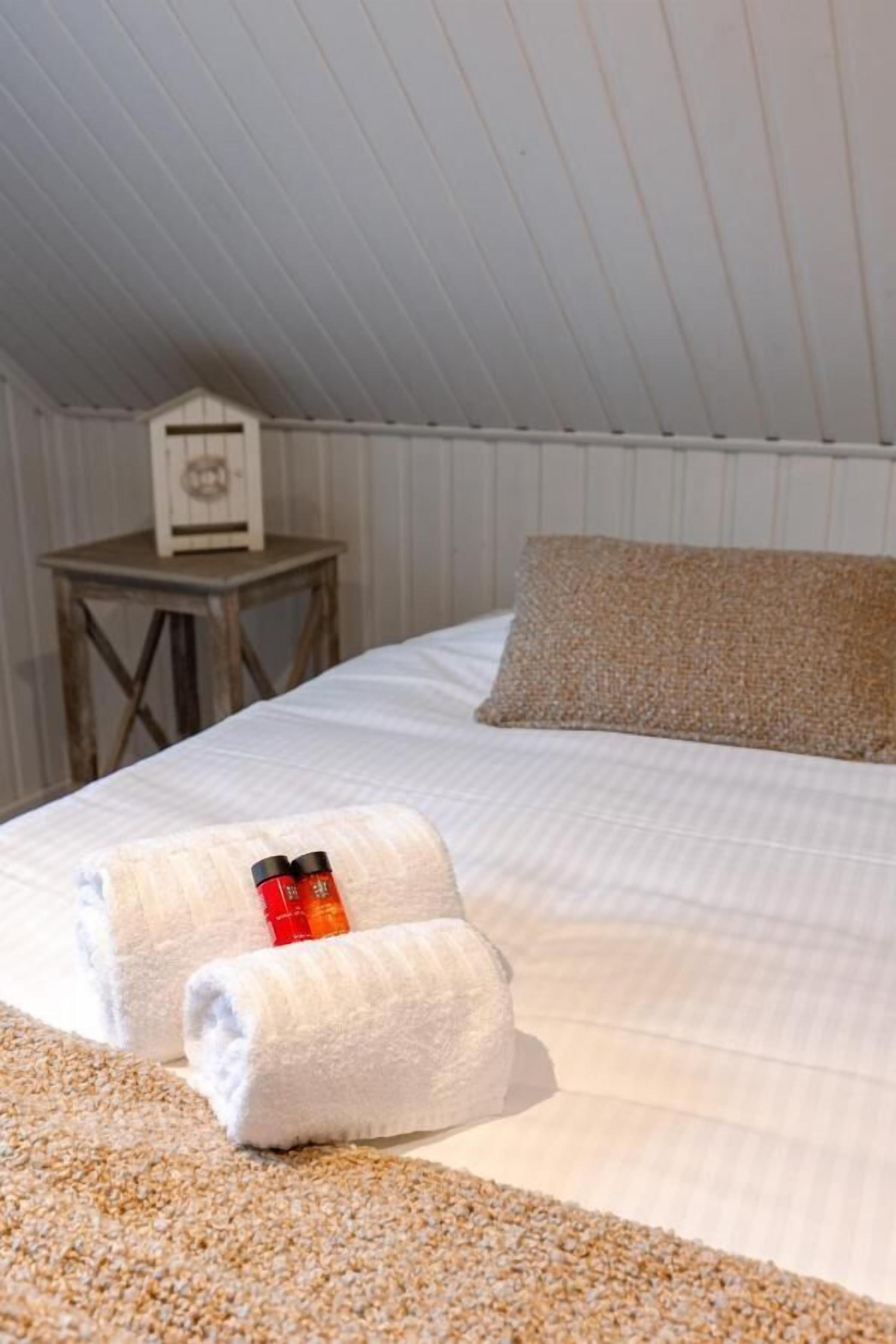 Un dormitorio con cama, almohadas y una mesita de noche con lámpara.