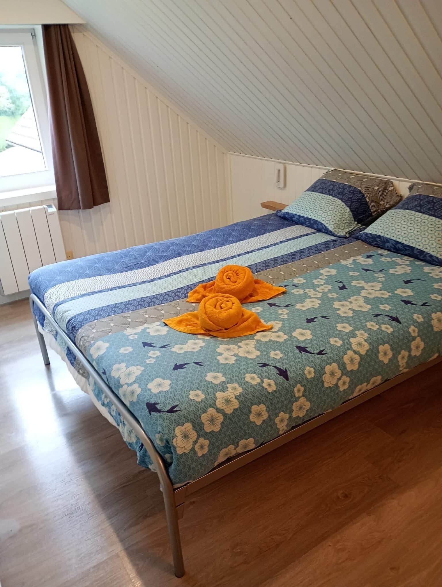 Een eenpersoonsbed met een bloemenprintdeken, twee kussens en twee opgerolde handdoeken op het bed.