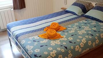 Een eenpersoonsbed met een bloemenprintdeken, twee kussens en twee opgerolde handdoeken op het bed.