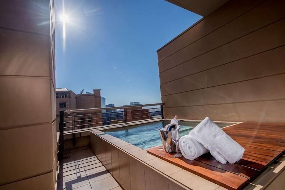 Een zwembad op het dak met uitzicht op de skyline van de stad, een houten terras en een jacuzzi met handdoeken.