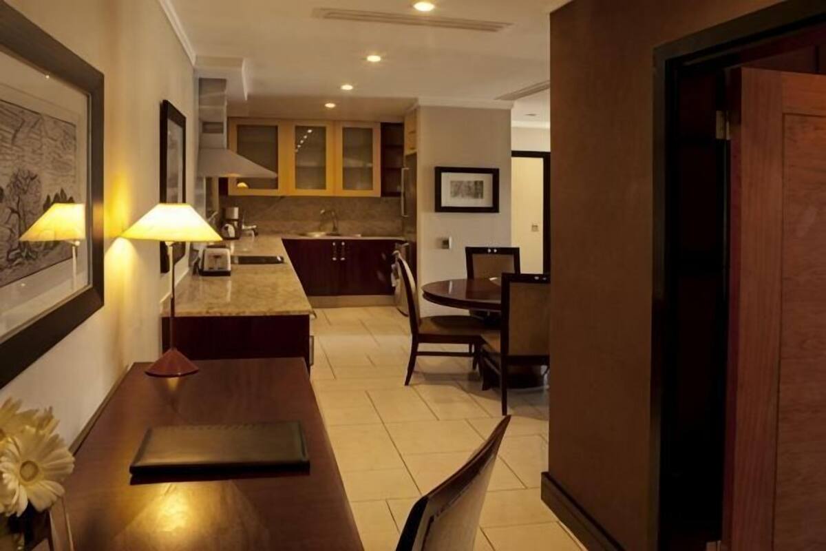 Een hotelkamer met een eettafel, stoelen, een kitchenette en een lijst met een afbeelding aan de muur.
