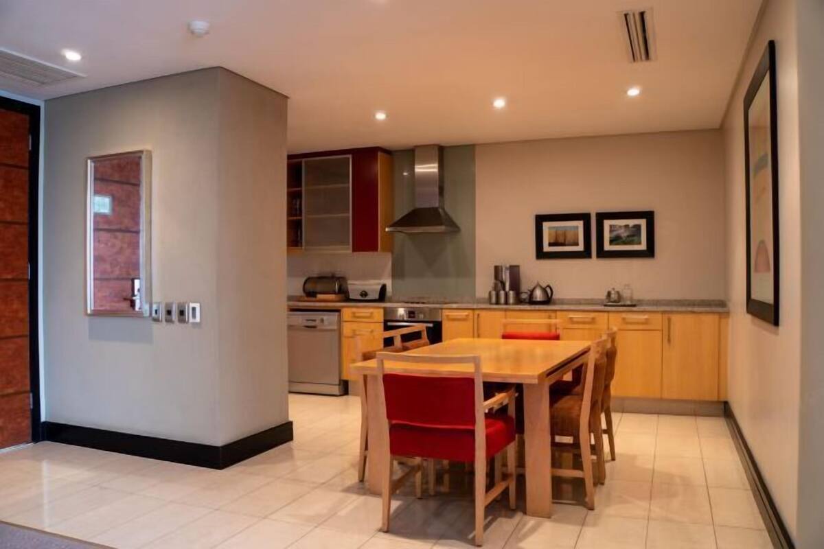 Een moderne keuken met een eethoek, met een houten tafel en stoelen, een inbouwoven en een RVS afzuigkap.