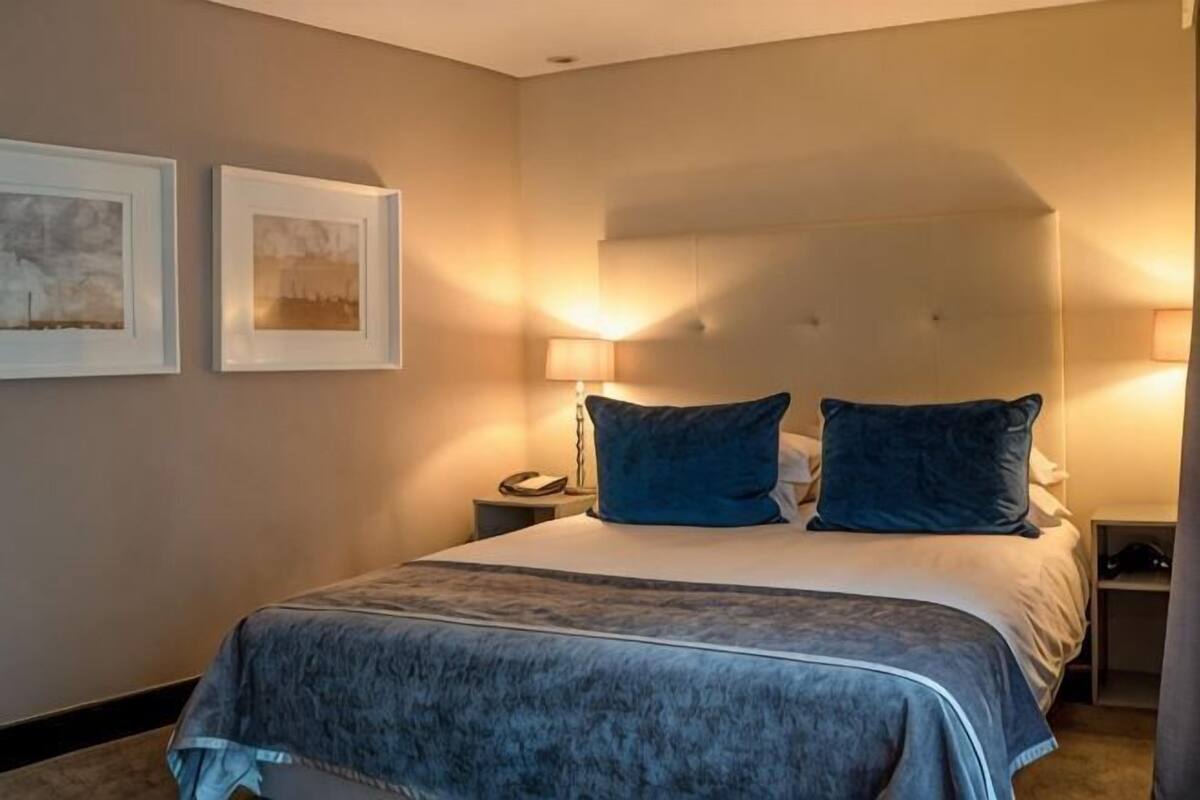 Een hotelkamer met een groot bed, twee bedlampen en twee ingelijste foto's aan de muur.
