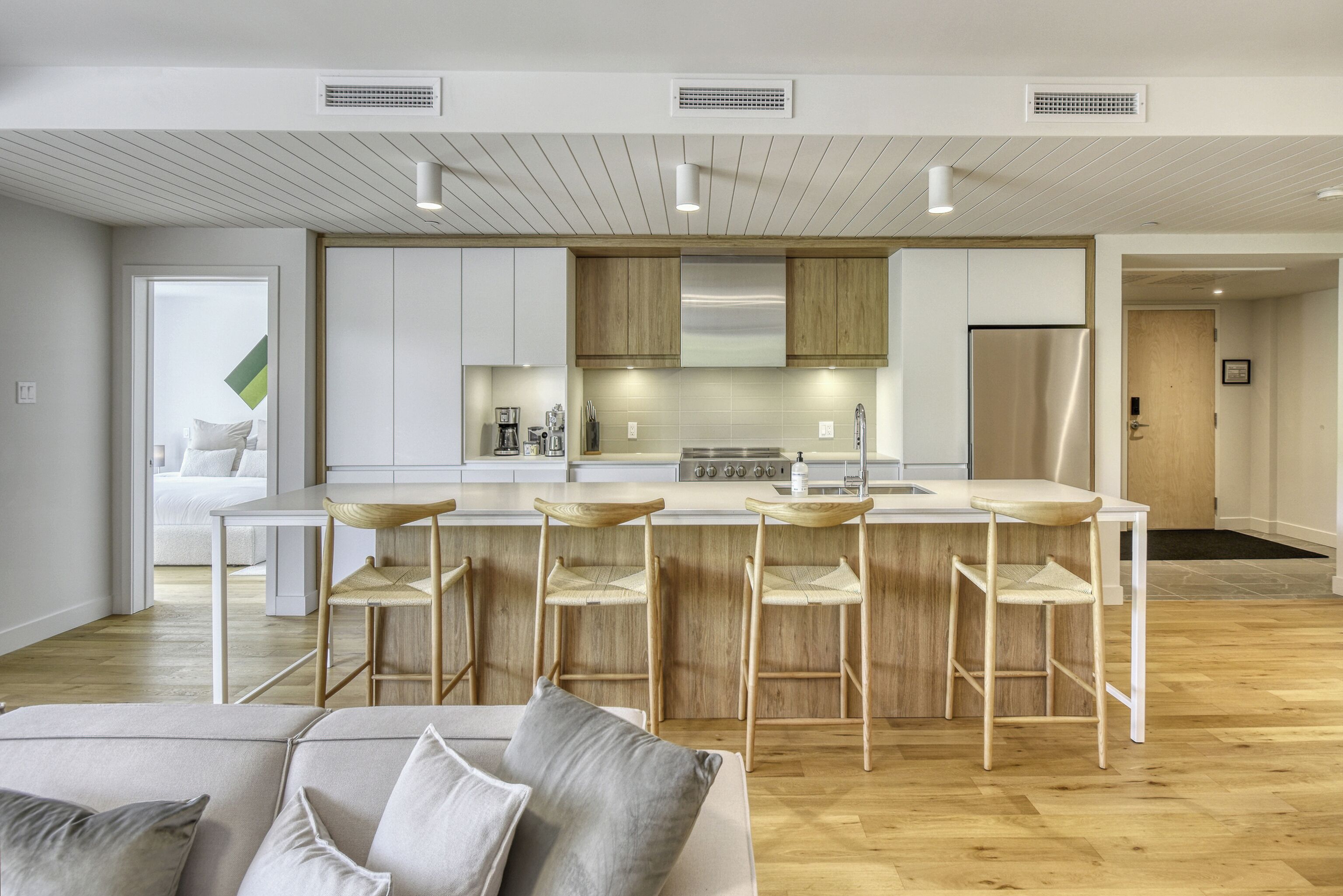 A modern kitchen with a central island, wooden bar stools, and a stainless steel refrigerator.