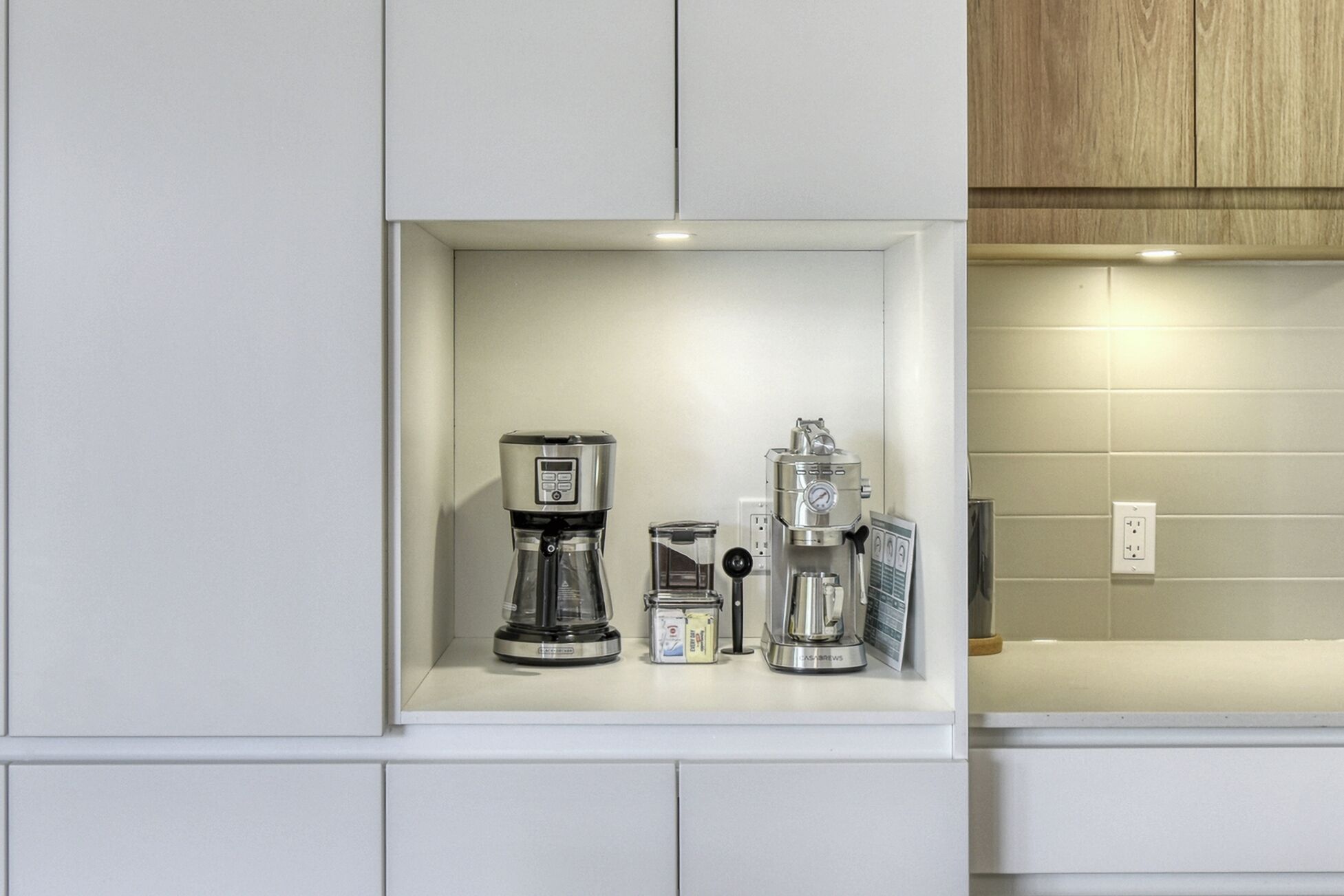 Une cuisine équipée d’un espace dédié à la préparation du café, comprenant une machine à café, un moulin et des récipients de rangement.