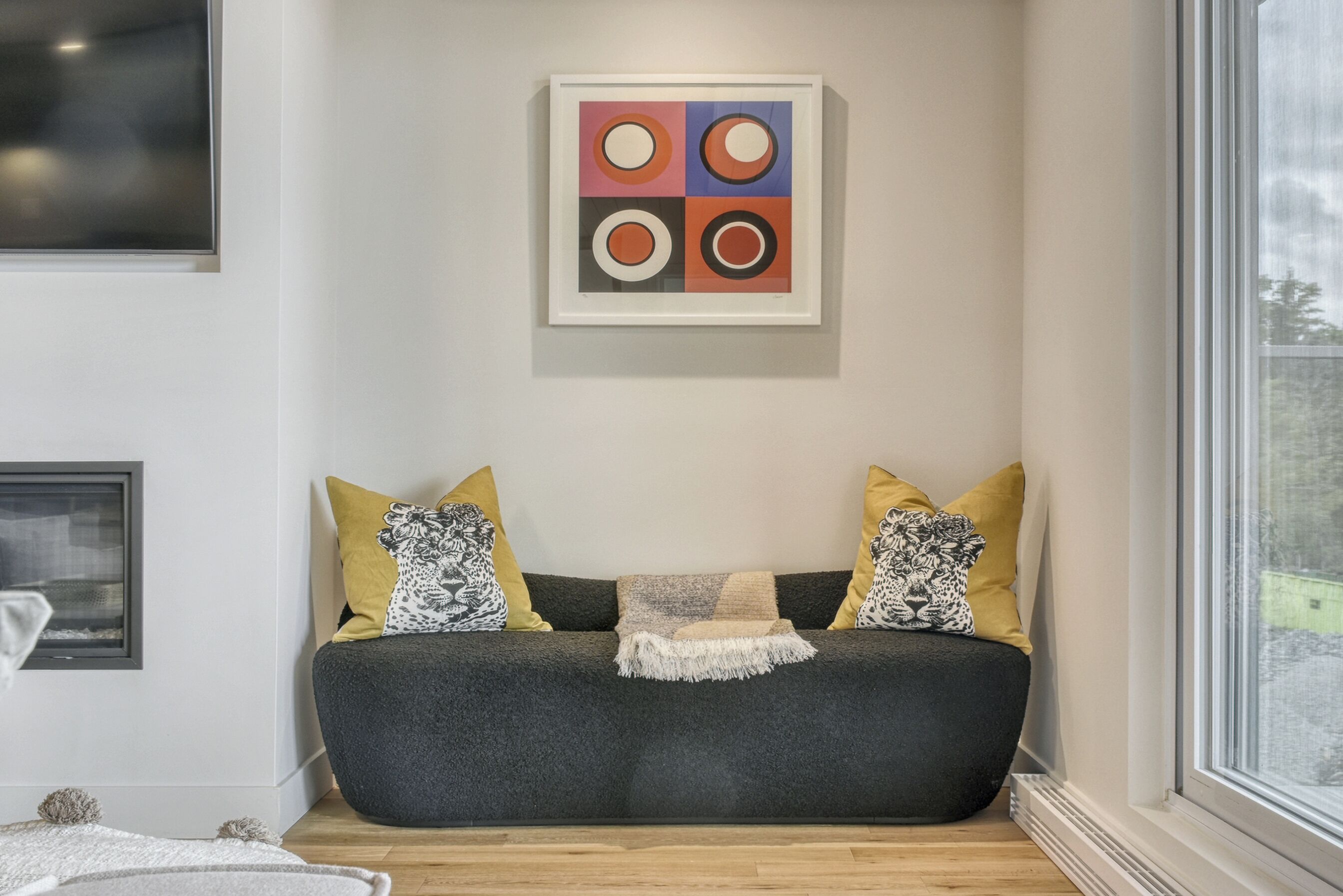 A modern living room with a dark grey sofa, yellow and black patterned cushions, and a framed abstract art piece above it.